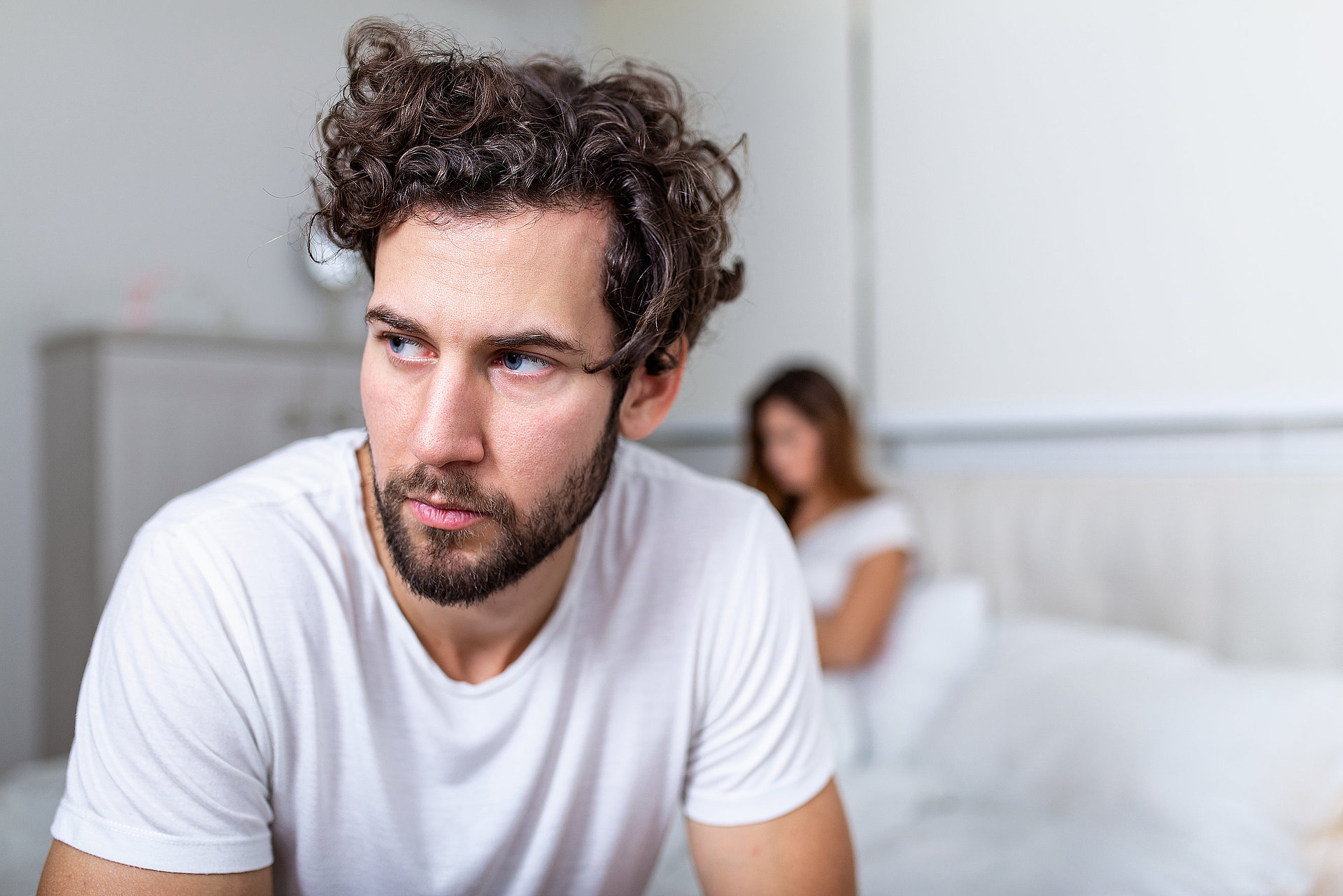 Sad thoughtful man after arguing with girlfriend.Relationship difficulties, conflict and family concept,unhappy couple having problems at bedroom. Sad guy sitting on bed,girlfriend in the background image-1471